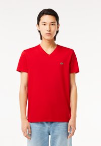 Rød v-hals t-shirt lavet af bomuld med korte ærmer; har et lille grønt Lacoste-logo på venstre bryst; glat tekstur.