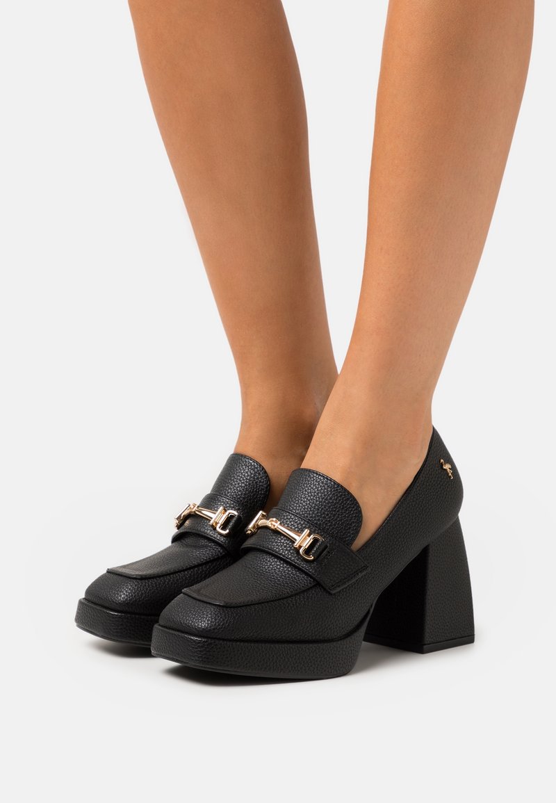 Mocassins en cuir noir à finition texturée, bout rond et détails en métal doré. Talon bloc épais pour plus de hauteur.