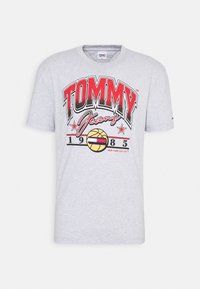 Vaaleanharmaa lyhythihainen T-paita, jossa on punainen ja musta "TOMMY Jeans 1985" -teksti sekä koripallografiikka, jossa on Tommy-lippu-logo.