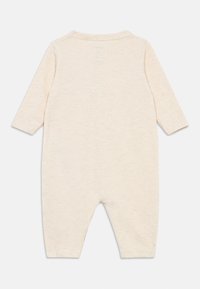 Macacão em tom de creme feito de um tecido macio e texturado. Apresenta mangas longas e um decote redondo. A vista traseira mostra um design simples, sem padrões.