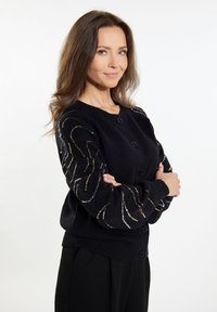 Cardigan nera in maglia con maniche lunghe, caratterizzata da motivi ondulati decorativi in paillettes sulle maniche e bottoni viola lungo il davanti.