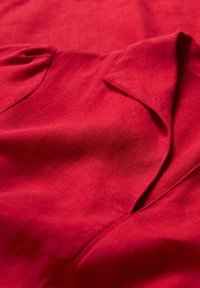 Roter Leinenstoff mit glatter Textur, subtiler Schattierung und drapierten Details, einschließlich eines Reverskragens und einer dezenten Taschenöffnung.