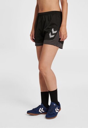 Person wearing black athletic shorts with gray trim and logo, black mid-calf socks, and blue sneakers with white chevron designs.