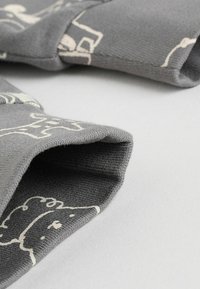 Grauener Stoff mit weicher Textur, der an den Kanten weiße abstrakte Muster aufweist. Das Design beinhaltet umgeschlagene Ärmel für einen geschichteten Look.