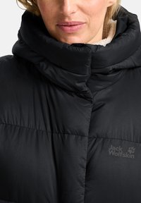 Zwarte pufferjack met hoge kraag, voorzien van gewatteerde panelen en een zachte binnenvoering. Toont het Jack Wolfskin-logo op de voorkant.