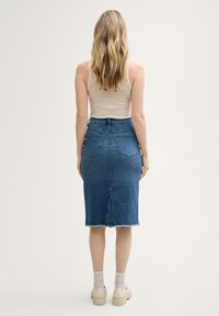 Denim pencil skirt in medium blue with a frayed hem. Features a mid-rise waist, two back pockets, and a straight fit. Styled with a beige tank top.