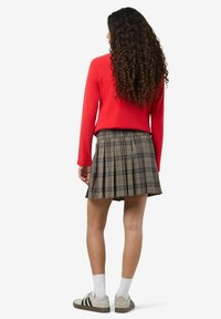 Top rosso a maniche lunghe abbinato a una gonna a pieghe grigia a quadri. Modella che indossa calze bianche e sneakers beige con righe nere.