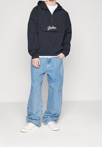Black pullover jacket with hood, front pocket, and white "Jordan" logo; paired with light blue baggy jeans and white sneakers.