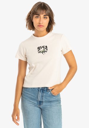 Cream short-sleeve t-shirt with embroidered black and green graphic design on chest. Cotton fabric with a relaxed, cropped fit. Blue denim jeans.