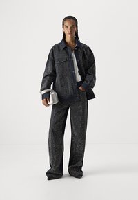 Chaqueta de denim azul marino y pantalones a juego con un patrón de puntos, tejido grueso, corte holgado y detalles en contraste; estilizados con un pequeño bolso de mano plateado.