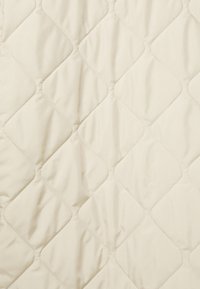 Cobija de edredón en tela beige claro con un patrón de diamantes, que muestra una textura suave y una costura uniforme en toda la superficie.