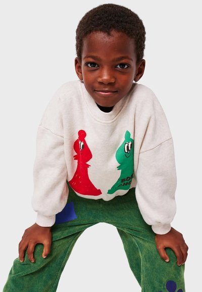 Felpa grigia chiara con stampe di pezzi degli scacchi a cartone animato in rosso e verde; abbinata a pantaloni in corduroy verde con toppe blu e viola.