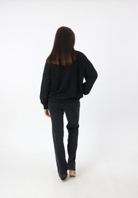Maglione nero oversize con maniche larghe abbinato a jeans grigi scuri e tacchi alti crema, visto da dietro.