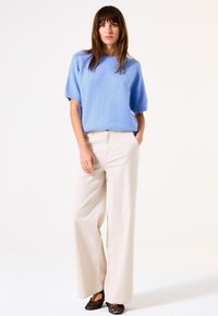 Hellblaues, kurzärmliges Sweatshirt und cremefarbene, weit geschnittene Hose. Strukturiertes Material mit lockerer Passform, kombiniert mit flachen Schuhen im dunklen Leopardenmuster.