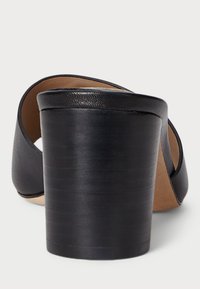 Fekete magassarkú szandál sima bőr felsőrésszel, nyitott hátsó résszel és kerek orral. Jellemzője egy magas, bordázott tömbsarok a stabilitás érdekében.