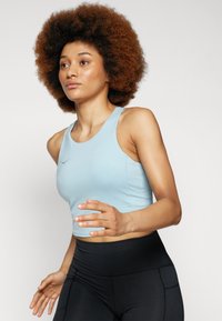 Svijetloplavi sportski crop top s glatkom teksturom, okruglim izrezom i uskim trakama, u kombinaciji s crnim tajicama visokog struka.