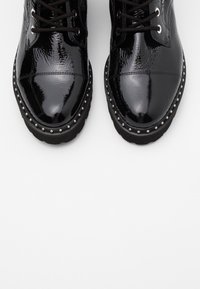 Bottines en cuir verni noir avec bout arrondi, fermeture à lacets et détails cloutés le long de la semelle. Finition brillante texturée.