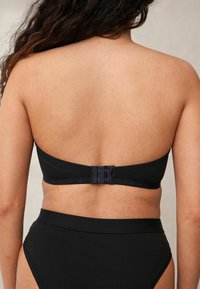 Zwarte strapless bikini-top met een gladde textuur, voorzien van een drievoudige haaksluiting aan de achterkant. Hoog-gesneden broekje met een nette afwerking.