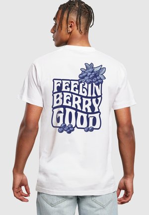 Balta kokvilnas T-kreklā ir zila grafiskā teksts "FEELIN BERRY GOOD" ar ogu ilustrācijām uz muguras. Īsas piedurknes, standarta piegriezums.