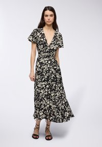 Abito maxi floreale nero con maniche a farfalla corte, scollo a V profondo, vita aderente e gonna fluida. Presenta motivi floreali bianchi e tessuto leggero.