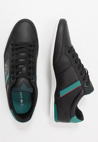 Musta urheilutennari, valmistettu keinonahasta. Ominaisuuksiin kuuluu turkoosit ja punaiset korostukset, teksturoitu verkkopaneeli sekä valkoinen pohja.