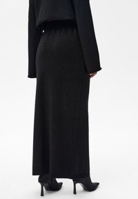 Czarna, długa dzianinowa spódnica z elastycznym pasem, wyróżniająca się gładką fakturą i subtelnym połyskiem; zestawiona z czarnymi szpilkami.