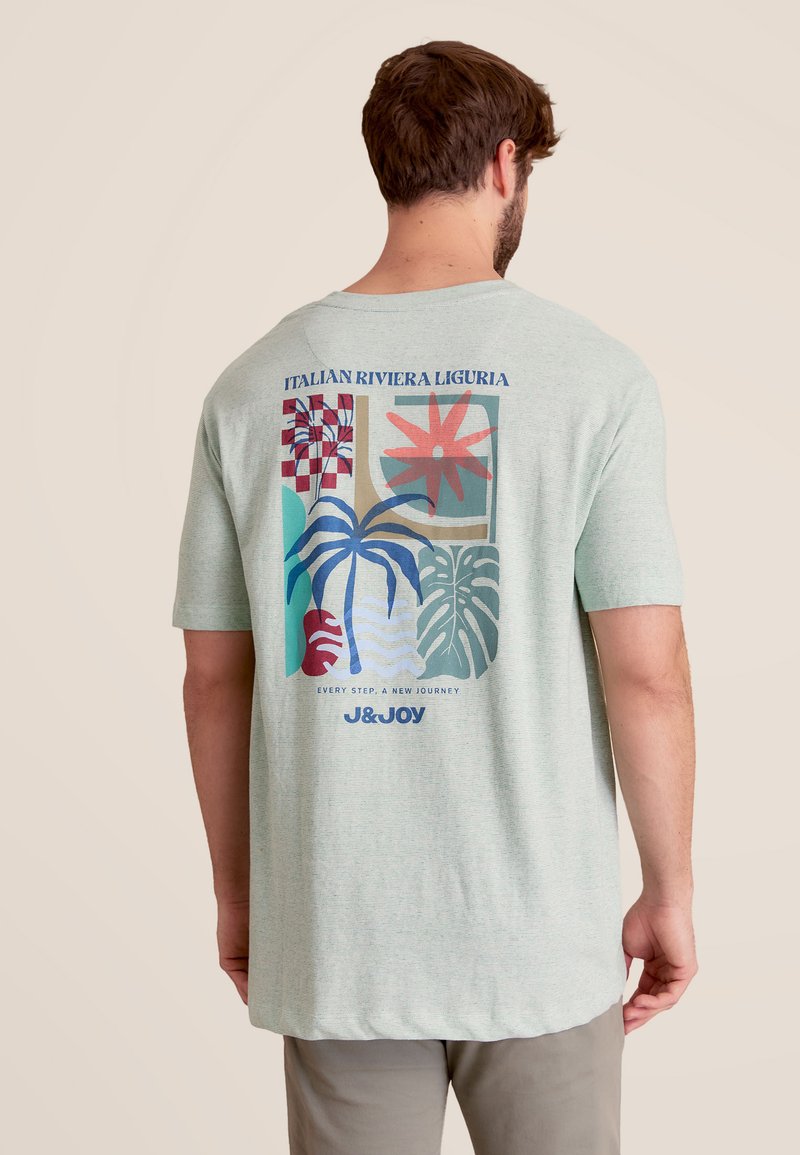 Lichtgroen T-shirt met korte mouwen en grafische print met kleurrijke planten en patronen. De tekst luidt "Italiaanse Rivièra Ligurië."