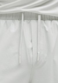 Pantalones jogger de color gris claro con una tela texturizada, cintura ajustable con cordones y un sutil patrón de cuadrícula.