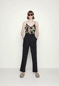 Calças pretas de cintura alta combinadas com um top floral preto com padrões em rosa e verde. Usadas com sandálias de deslizar e óculos de sol.