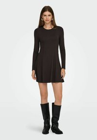 Vestito nero a maniche lunghe con corpino attillato e orlo svasato, realizzato in tessuto liscio. Indossato con stivali neri di pelle al ginocchio.