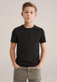 Černé krátké tričko z bavlny s kulatým výstřihem a volnějším střihem, doplněné olivově zelenými kalhotami.