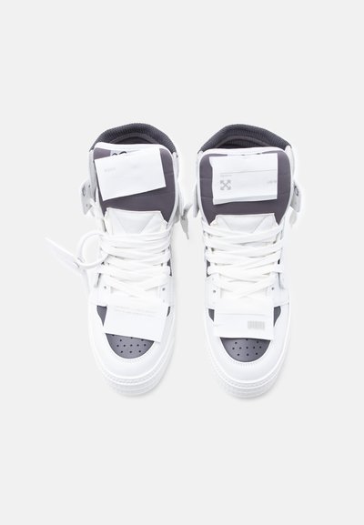 Ζευγάρι λευκά και μαύρα ψηλά αθλητικά παπούτσια με λευκά κορδόνια, τοποθετημένα δίπλα-δίπλα σε λευκό φόντο, από ψυχρή οπτική γωνία.