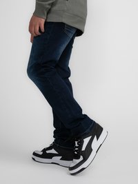 Tmavě modré džínové kalhoty s úzkým střihem, kombinované s černobílými vysokými teniskami s kontrastními akcenty a texturovanými panely.