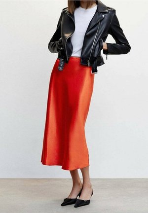 Veste de motard en cuir noir, T-shirt blanc, et jupe midi fluide en satin rouge, associée à des ballerines pointues noires. Textures lisses, coupe ajustée.