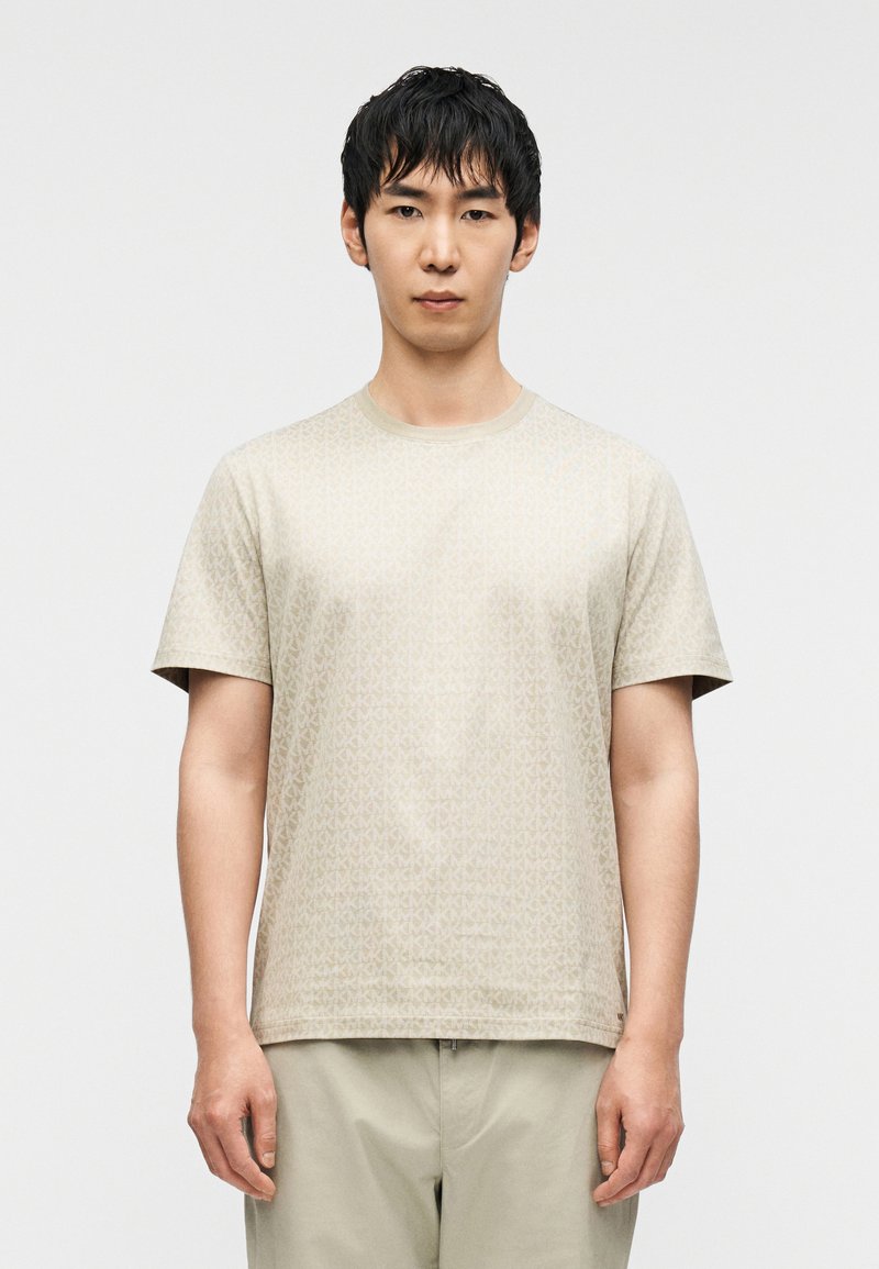 T-shirt beige à manches courtes avec un motif géométrique subtil, encolure ronde et texture douce, associé à un pantalon de couleur claire.