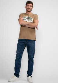 Kaki bomuld t-shirt med et grafisk print i grøn og hvid; parret med mørkeblå denim jeans og hvide sneakers.