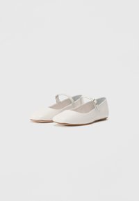 Vita patentläderballerinas med spetsig tå, justerbar ankelrem och platt sula, med en slät, glänsande yta.