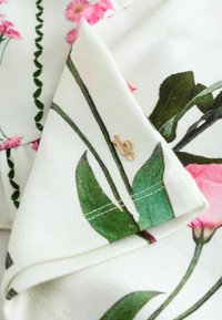 Bloemmotief stof in het wit, met roze bloemen en groene bladeren, met een klein gouden accentlabel waarop het nummer 10 staat.