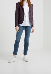 Lila rutmönstrad blazer, vit skjorta, blå slim-fit byxor och vita sneakers. Blazern har två knappar och slagkragar.