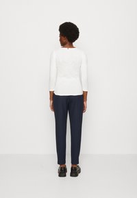 Maglietta bianca a maniche lunghe con scollatura rotonda, abbinata a pantaloni blu navy e scarpe nere, caratterizzata da trame lisce e una vestibilità rilassata.