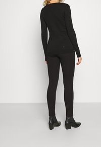 Svart långärmad topp med rundad halsringning, i kombination med tajta svarta leggings och svarta klackade ankelstövlar. Enkelt och figursytt mönster.