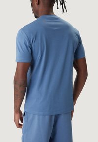 Maglietta in cotone blu con maniche corte, scollo rotondo e texture liscia. Presenta una vestibilità comoda e un design semplice senza loghi visibili.