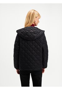 Czarna pikowana kurtka puchowa z kapturem, z obszyciem w romby i luźnym krojem, noszona na czerwonym kołnierzu.