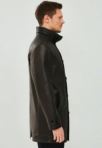 Zwarte leren jas met een gestructureerde afwerking, hoge kraag, zijzakken en knoopsluitingen, gezien vanuit een profielweergave.