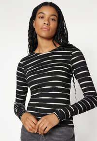 Long-sleeve top in black with horizontal white stripes, made of ribbed fabric. Features a round neckline and fitted design.
