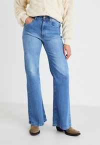 Jeans a vita alta svasati in denim azzurro chiaro, con cinque tasche, chiusura con bottone e leggero effetto sbiadito per aggiungere texture.