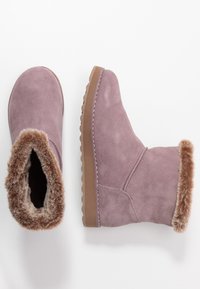Fialové semišové kotníkové boty s umělou kožešinou uvnitř a texturovanou podrážkou. Mají zaoblenou špičku a střední výšku.