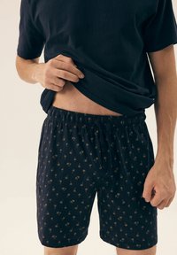 Granatowe szorty w wzory z małymi motywami palm, z elastycznym pasem i sznurkiem, wykonane z miękkiej tkaniny.