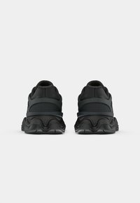 Sapatos atléticos pretos com um upper de malha texturizada, sola acolchoada com um design ondulado e calcanhar reforçado para estabilidade.