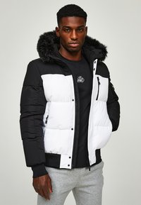 Padded jacket with a black and white color block design, featuring a fur-lined hood, zippered pockets, and a textured fabric finish.